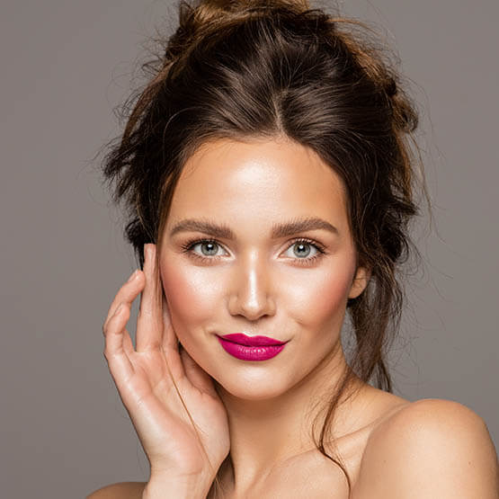 Beauty portrait of attractive smiling female with a brunette messy bun touching cheek with bright pink lipstick
